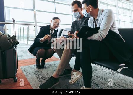 Assistente di terra che assiste la coppia che siede all'aeroporto durante la pandemia di covid-19. Uomo e donna in maschere di faccia ottenere aiuto dal personale dell'aeroporto in attesa Foto Stock