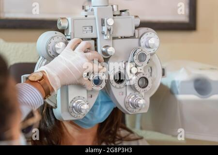 Giovane donna alla nomina dell'oftalmologo. Controllo della vista. Un oftalmologo guanto regola il dispositivo. Primo piano. Foto Stock
