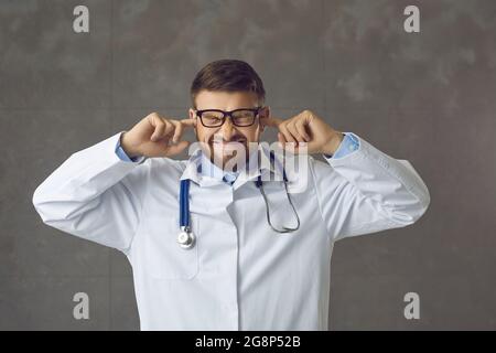 Il medico stressato e infastidito chiude le orecchie con le dita cercando di ignorare i rumori forti dell'ospedale Foto Stock