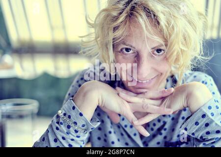 Ritratto di una giovane donna caucasica matura con capelli biondi in casa sorridente. Foto Stock