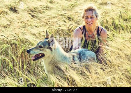 ritratto di una giovane donna caucasica matura con il suo cane da lupo all'aperto in un paesaggio di cereali. Concetto di stile di vita. Foto Stock