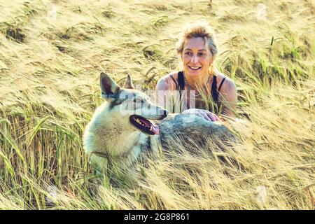 ritratto di una giovane donna caucasica matura con il suo cane da lupo all'aperto in un paesaggio di cereali. Concetto di stile di vita. Foto Stock