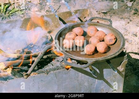 Falafel cuocete in una padella all'aperto. Fuoco di legno preparato per grigliare sulla natura. Picnic. Stagione grigliata in natura aperta. Foto Stock