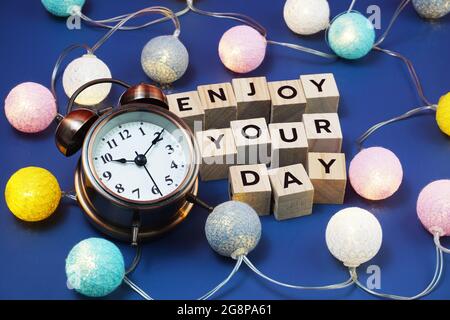 Goditi le lettere alfabetiche della giornata con sveglia e decorazioni in batuffoli di cotone a LED su sfondo blu Foto Stock