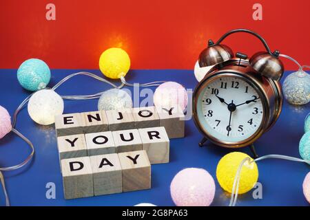 Goditi le lettere alfabetiche della giornata con sveglia e decorazioni in batuffoli di cotone a LED su sfondo blu Foto Stock