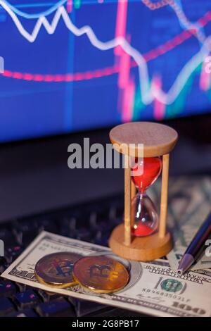 clessidra, dollari e monete di bit su una tastiera di computer sullo sfondo di grafici Foto Stock