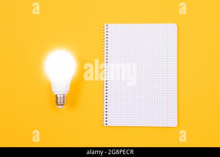 Un concetto di idea - UNA lampada a risparmio energetico e UN blocco note giacenti su un tavolo giallo. Vista dall'alto, disposizione piatta, modello vuoto Foto Stock