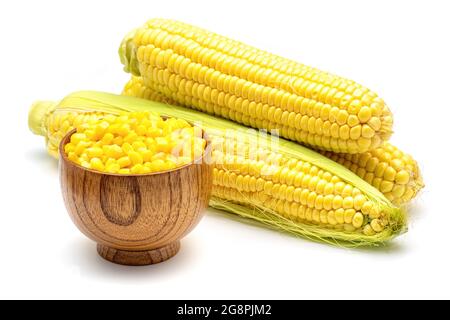 Cereali di mais dolci in una ciotola di legno sullo sfondo di pannocchie di mais fresche. Chicchi di mais dolci freschi e pannocchie di mais isolate su sfondo bianco. Foto Stock