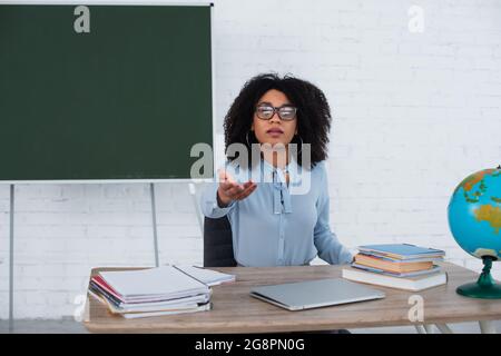 Insegnante afroamericano che punta con la mano vicino al computer portatile e notebook in classe Foto Stock