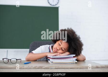 Studente afroamericano che dorme sui taccuini vicino agli occhiali in classe Foto Stock