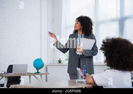 Insegnante afroamericano che punta con la mano vicino allievo offuscato in classe Foto Stock