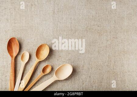 Cucchiai artigianali fatti da diversi tipi di legno giacciono in fila su un tessuto di tela di canapa Foto Stock