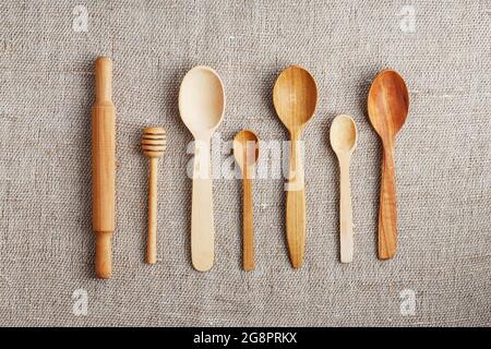 Cucchiai artigianali fatti da diversi tipi di legno giacciono in fila su un tessuto di tela di canapa Foto Stock