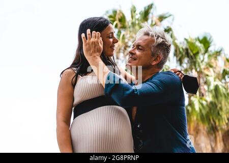 Coppia, con la donna incinta, guardando gli occhi l'un l'altro e in posa per una foto durante la vacanza estiva nel giardino esotico dopo coronavirus oubr Foto Stock