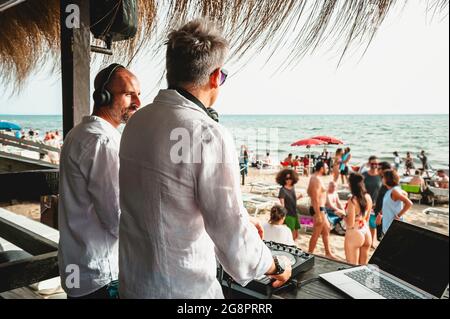 Disc jockeys che suona musica per i turisti al club party all'aperto sulla spiaggia - DJ indossando le cuffie all'evento musicale dal vivo - Musica e concetto di divertimento Foto Stock