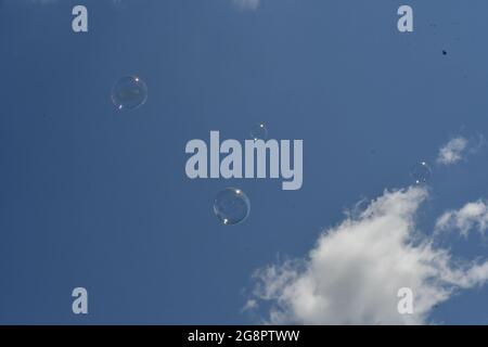 Quattro bolle che galleggiano contro un cielo azzurro con nuvole che passano Foto Stock