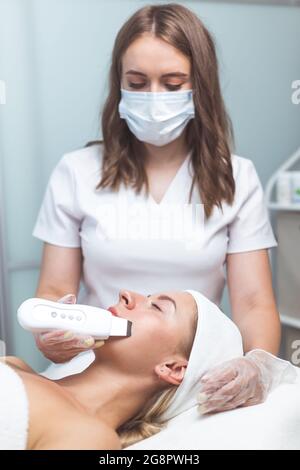 Il cosmetologo professionista usa la fonoforesi per pulire il volto di una cliente femminile. Bellezza e salute della pelle Foto Stock