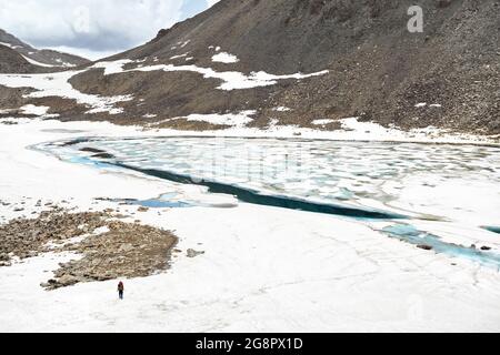 Bellissimo scenario del lago di montagna ghiacciaio blu con pezzi di ghiaccio all'interno e piccolo escursionista in Kazakistan. Foto Stock