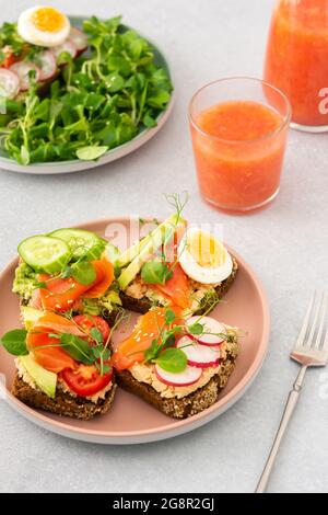 Sana e gustosa colazione, panini con avocado e salmone, cetrioli e pomodori, ravanelli e micrograni di piselli con uova sode e insalata di radice Foto Stock