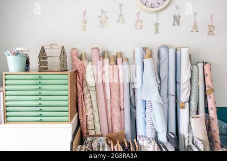 Rotoli di tessuti di colori diversi all'interno di un'officina di moda luminosa accanto ad altre attrezzature. Foto Stock