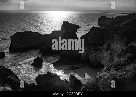 Vista panoramica della spiaggia, le scogliere formano una piccola baia, un uomo cammina nelle ombre in lontananza. Portogallo, Alvor Foto Stock