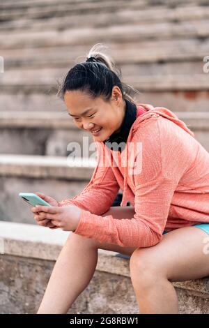 Giovane donna che usa il suo telefono cellulare dopo l'esercizio. Indossa abiti sportivi e cuffie. Foto Stock