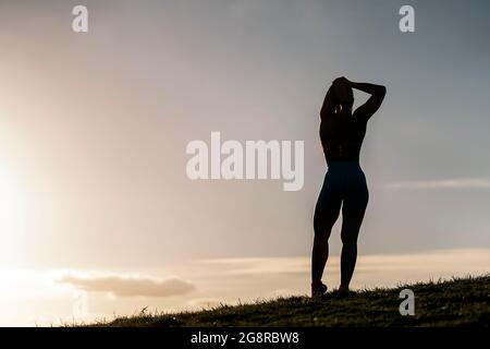 Donna non riconosciuta che indossa abiti sportivi che si allungano nel parco dopo essersi allenata la sera. Foto Stock