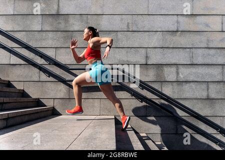 Donna asiatica forte con abiti sportivi che si allenano in città durante il giorno di sole. È scalata. Foto Stock