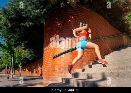 Giovane donna attiva con abiti sportivi che corrono in città e allenarsi. Indossa le cuffie e ascolta la musica. Foto Stock