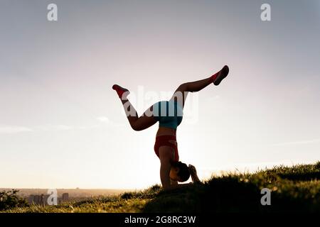 Donna non riconosciuta che indossa abiti sportivi facendo posa yoga e allenarsi nel parco. È forte e flessibile. Foto Stock