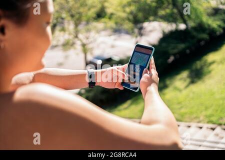 Donna attiva non riconosciuta con abiti sportivi utilizzando il suo telefono cellulare e controllare il suo allenamento. Foto Stock
