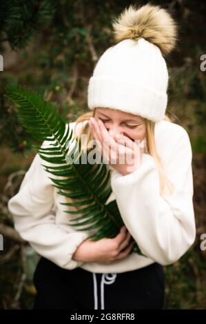 Ragazza adolescente in cappello invernale che tiene verde Fern mentre Laughing Foto Stock