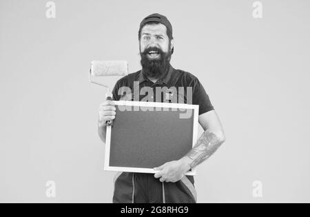 Pronto al lavoro. Idea creativa. Caposquadra pubblicizza il servizio di parete di fronte. Uomo felice con spazio di copia del bordo. Hipster maturo uso strumento rullo di vernice per Foto Stock