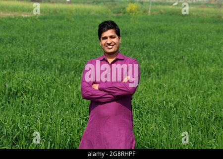 preoccupatevi di meno, agricoltore indiano in piedi piegato a mano nel suo campo di grano sano e sboccando Foto Stock