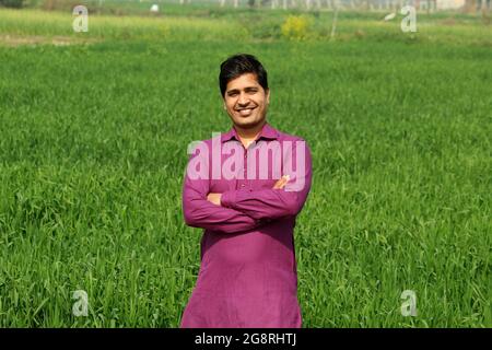 preoccupatevi di meno, agricoltore indiano in piedi piegato a mano nel suo campo di grano sano e sboccando Foto Stock