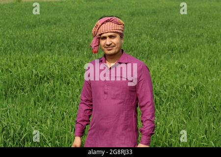 preoccupatevi di meno, agricoltore indiano in piedi piegato a mano nel suo campo di grano sano e sboccando Foto Stock