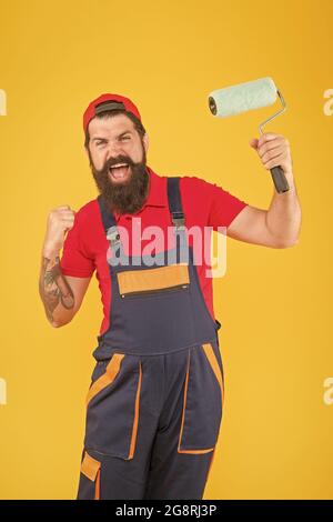 felice uomo brutale in uniforme di boilersuit. hipster maturo uso rullo di vernice strumento per la pittura. repairman o costruttore di lavoro. idea creativa. caposquadra andare Foto Stock