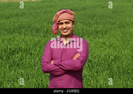 preoccupatevi di meno, agricoltore indiano in piedi piegato a mano nel suo campo di grano sano e sboccando Foto Stock