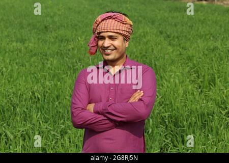 preoccupatevi di meno, agricoltore indiano in piedi piegato a mano nel suo campo di grano sano e sboccando Foto Stock