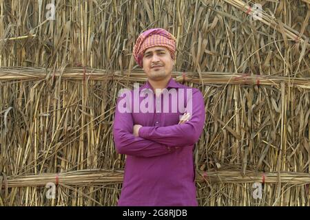 preoccupatevi di meno, agricoltore indiano in piedi piegato a mano nel suo campo di grano sano e sboccando Foto Stock