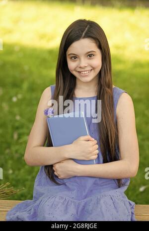 Piccola ragazza intelligente con libro all'aperto giorno di sole, concetto di poesia romantica Foto Stock