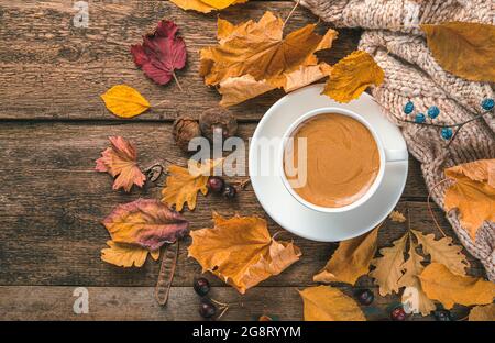 Una tazza di cappuccino, un maglione e fogliame autunnale su sfondo ligneo. Sfondo autunno festivo. Spazio per la copia. Foto Stock