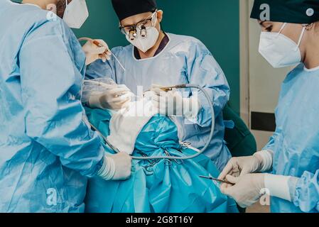 Operatori medici che eseguono interventi chirurgici all'interno della sala operatoria dell'ospedale - Focus sulle mani del medico del centro Foto Stock