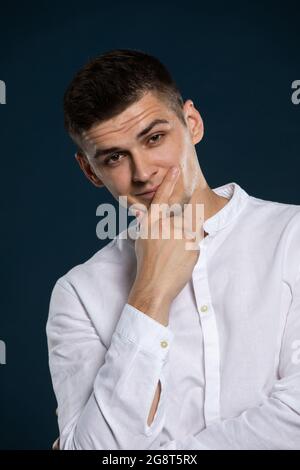 Ritratto di un giovane bell'uomo che indossa una camicia bianca a maniche lunghe. Sta guardando avanti. Foto Stock