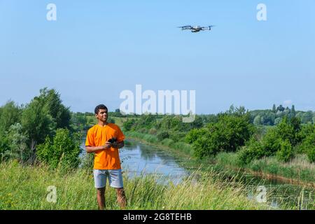 Uomo afroamericano che opera con il drone con il controller in mani sul prato Foto Stock