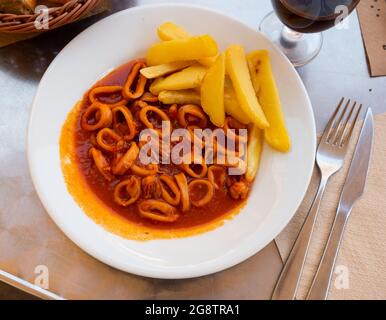 Anelli di calamari stufati in americaina salsa servita con patatine fritte Foto Stock