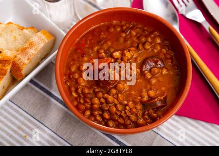 Lenticchie stufate con chorizo e verdure in ciotola di terracotta Foto Stock