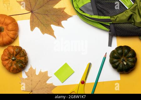 Zaino, forniture scolastiche, foglie d'arancia e zucche su sfondo giallo. Biglietto d'auguri per il giorno degli insegnanti Foto Stock