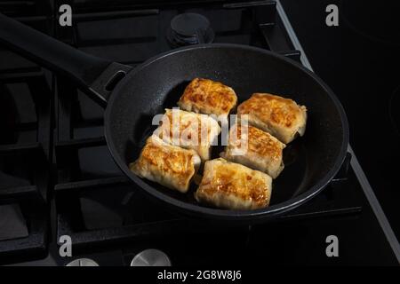 Processo di cottura fatti in casa involtini di cavolo ripieni. Pochi panini vengono fritti su una padella e su una stufa da cucina nera. I panini appena fritti sono coperti Foto Stock