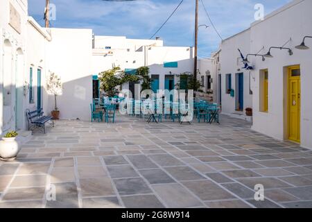 Isola di Serifos, Chora, Cicladi Grecia. Strada acciottolata tradizionale aperto vuoto taverna bianca caffetteria con tavoli in metallo, poltrone in vimini blu sedile b Foto Stock